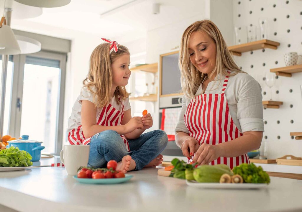 Eine Mutter und ihre Tochter stehen in der Küche und bereiten Essen zu.